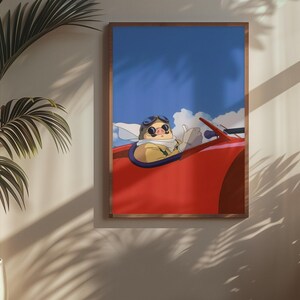 May include: A framed art print featuring an animated character in a red convertible against a blue sky with clouds. The character wears goggles and a scarf. The artwork is displayed on a wall with a potted plant.