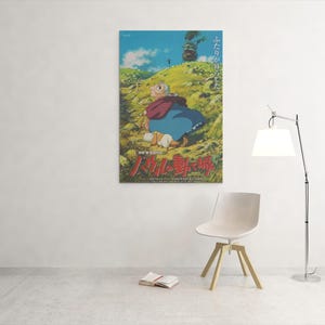 May include: A framed poster featuring a scene from an animated film. The artwork depicts a character in a red cloak and blue dress sitting on a grassy hill. Japanese text is visible at the bottom of the poster.