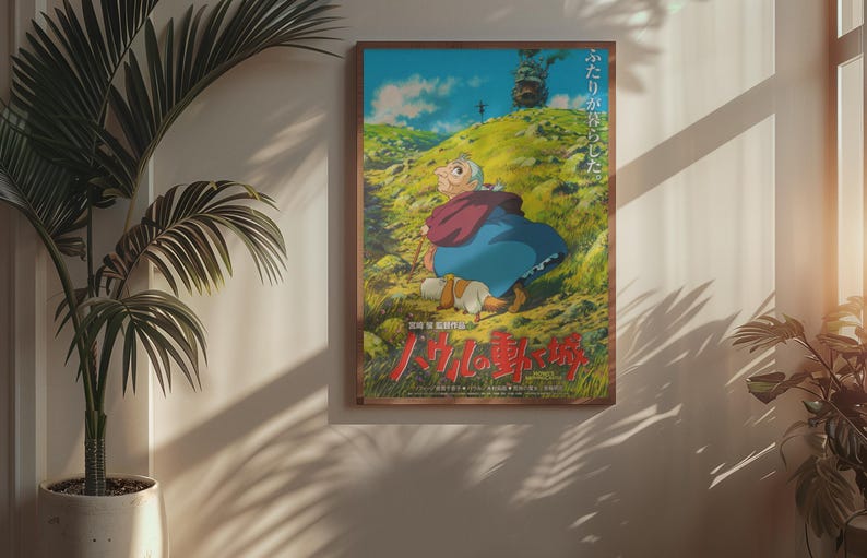 May include: Framed poster featuring an animated character in a blue dress and red shawl, walking on a green hillside. The poster has Japanese text and is set in a wooden frame. A potted plant is in the foreground.