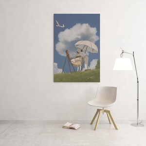 May include: A framed print depicts a person painting outdoors under a white umbrella. The artwork features a blue sky with fluffy clouds, a grassy hill, and a flying bird. The scene is set against a white wall with a modern chair and lamp.