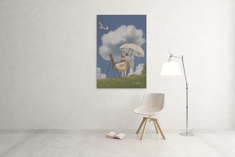 May include: A framed print depicts a person painting outdoors under a white umbrella. The artwork features a blue sky with fluffy clouds, a grassy hill, and a flying bird. The scene is set against a white wall with a modern chair and lamp.