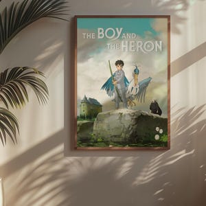 May include: Framed poster featuring artwork from "The Boy and the Heron." The image depicts a boy with a staff and a heron-like creature standing on a rock. A castle and a black figure are in the background. The title is displayed at the top.