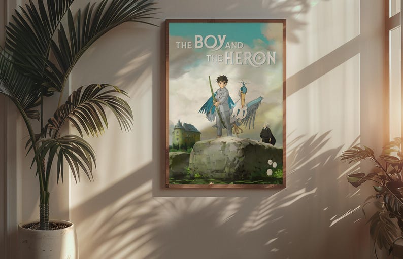 May include: Framed poster featuring artwork from "The Boy and the Heron." The image depicts a boy with a staff and a heron-like creature standing on a rock. A castle and a black figure are in the background. The title is displayed at the top.