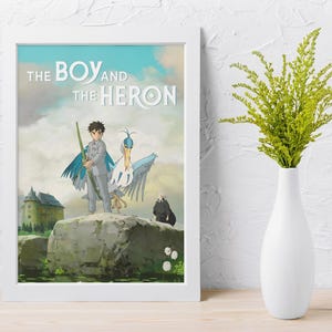 May include: A framed art print featuring the title "The Boy and the Heron" with a cartoon illustration. The artwork depicts a boy with a heron, a castle, and a dark figure. The frame is white, and the background is a cloudy sky.