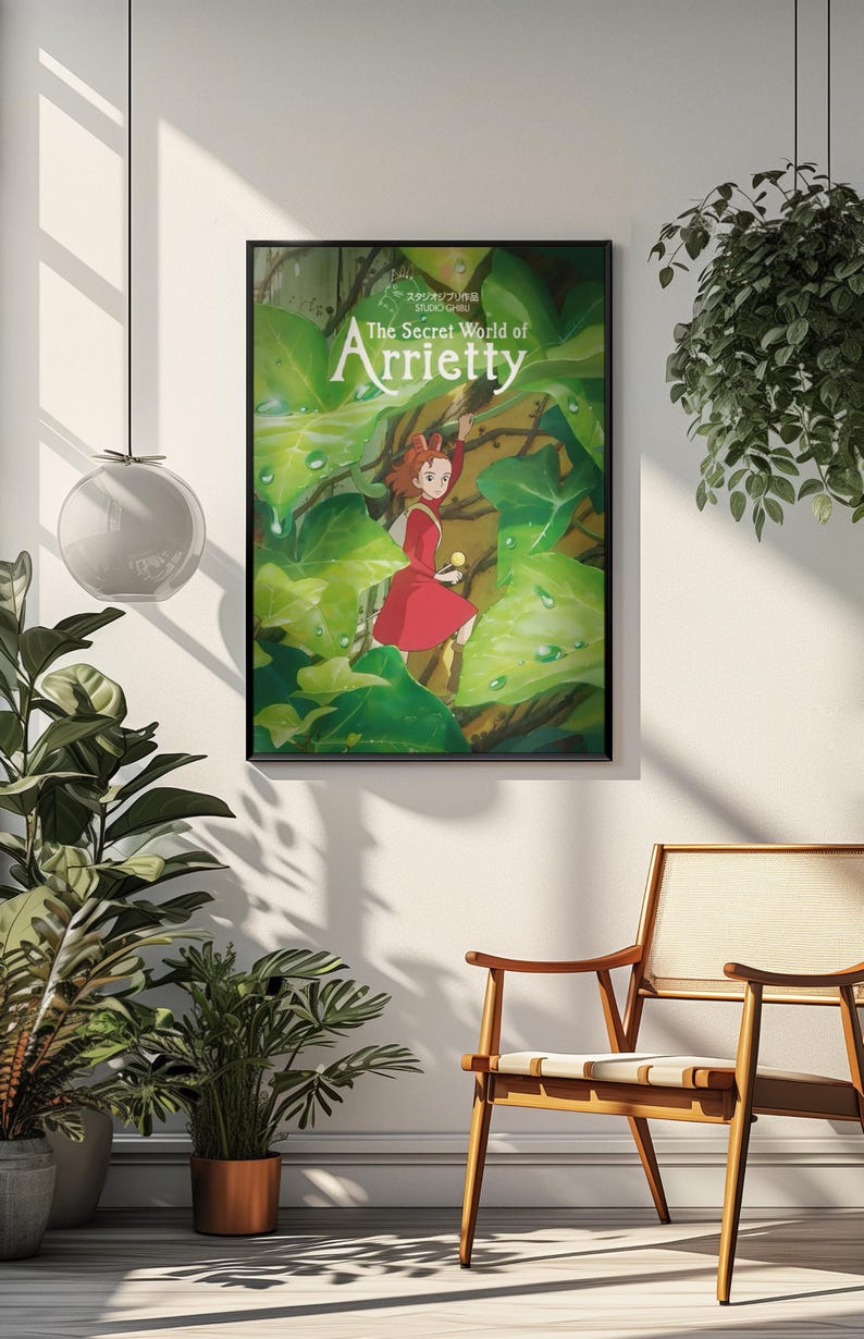 May include: Framed poster featuring the animated film "The Secret World of Arrietty." The artwork depicts a young girl in a red dress amidst large green leaves. The poster is in a black frame, hanging on a white wall.