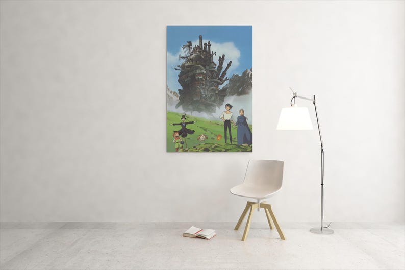May include: A framed art print featuring a scene from the animated film "Howl's Moving Castle." The artwork depicts a large, moving castle, characters, and a green landscape under a blue sky. The print is displayed on a white wall.