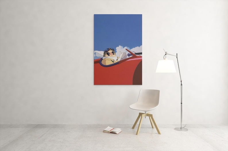 May include: A framed art print depicts a cartoon character in a red vintage car against a blue sky with clouds. The character wears goggles and a scarf. The print hangs on a white wall.