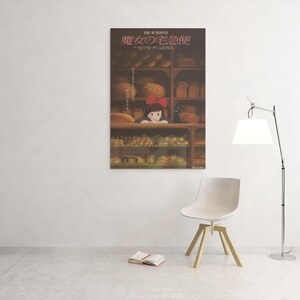 May include: A poster featuring a scene from the animated film, Kiki's Delivery Service, hangs on a white wall. The poster shows a young girl with a red bow in a bakery. A white chair, a lamp, and a book are in the room.