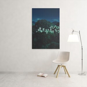 May include: A framed canvas art print depicting a dark, lush landscape with white, glowing floral shapes under a starry night sky. A modern white chair with wooden legs, a floor lamp, and an open book are in the foreground.
