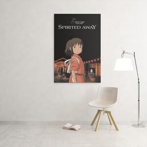 Puede incluir: Un p&oacute;ster enmarcado de la pel&iacute;cula de animaci&oacute;n "El viaje de Chihiro" cuelga de una pared blanca. El p&oacute;ster muestra a una joven con un vestido naranja, con el t&iacute;tulo de la pel&iacute;cula en blanco. Una silla blanca y una l&aacute;mpara de pie est&aacute;n delante.