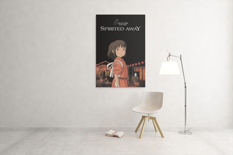 Puede incluir: Un p&oacute;ster enmarcado de la pel&iacute;cula de animaci&oacute;n "El viaje de Chihiro" cuelga de una pared blanca. El p&oacute;ster muestra a una joven con un vestido naranja, con el t&iacute;tulo de la pel&iacute;cula en blanco. Una silla blanca y una l&aacute;mpara de pie est&aacute;n delante.