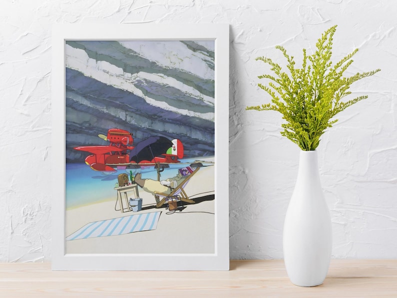 Peut inclure: Impression d'art encadr&eacute;e repr&eacute;sentant un hydravion rouge, une personne se relaxant dans une chaise longue sous un parasol et une serviette de plage ray&eacute;e. L'arri&egrave;re-plan montre une falaise rocheuse et de l'eau bleue. Un vase blanc avec des plantes vertes est &agrave; droite.