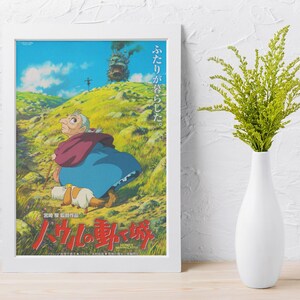 May include: Framed poster featuring a scene from an animated film. The artwork depicts a character in a blue dress and red shawl, walking with a dog on a grassy hill. A castle with smoke is in the background. Japanese text is at the bottom.