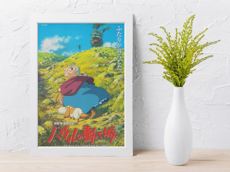 May include: Framed poster featuring a scene from an animated film. The artwork depicts a character in a blue dress and red shawl, walking with a dog on a grassy hill. A castle with smoke is in the background. Japanese text is at the bottom.