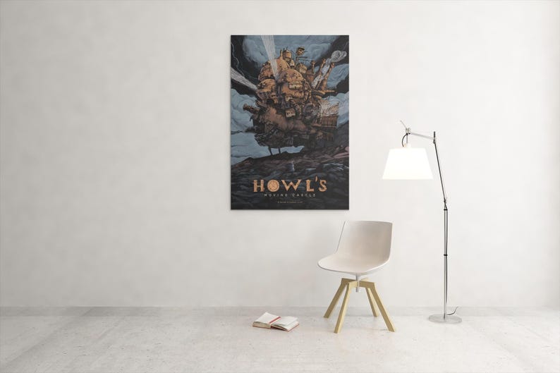May include: A framed poster of Howl's Moving Castle hangs on a white wall. The artwork depicts the castle in a cloudy sky. Below the castle is the title "Howl's Moving Castle" in gold lettering. A white chair and a floor lamp are in front of the wall.
