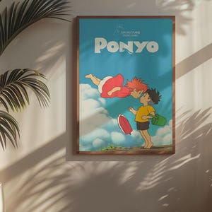 May include: A framed poster featuring the animated film "Ponyo." The artwork depicts two characters kissing, with the title "PONYO" in large white letters against a blue sky background. The poster is in a wooden frame and hangs on a wall.