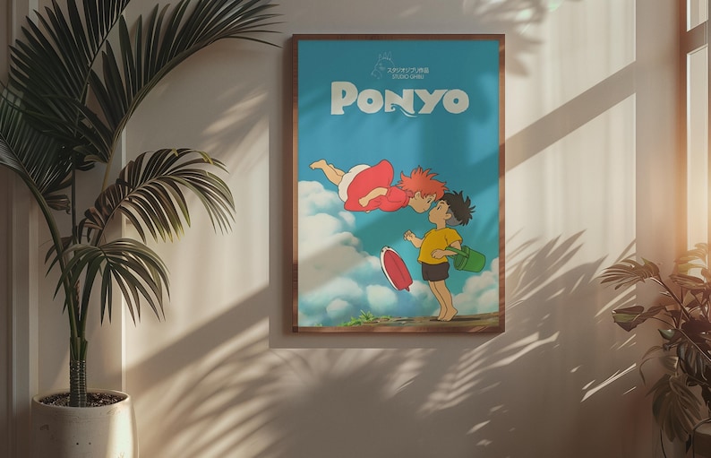 May include: A framed poster featuring the animated film "Ponyo." The artwork depicts two characters kissing, with the title "PONYO" in large white letters against a blue sky background. The poster is in a wooden frame and hangs on a wall.
