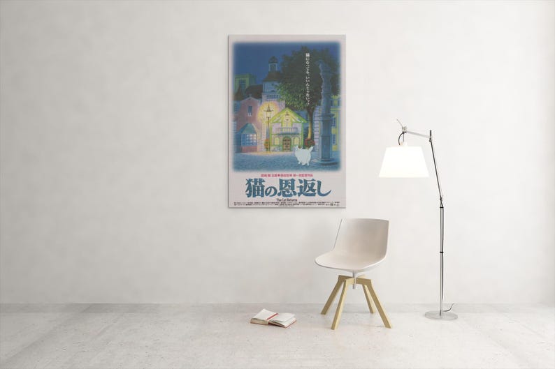 Puede incluir: Un p&oacute;ster enmarcado con texto japon&eacute;s, que representa una escena callejera nocturna con edificios y un gato blanco. El p&oacute;ster est&aacute; en una pared blanca. Una silla moderna, un libro y una l&aacute;mpara est&aacute;n en la habitaci&oacute;n.