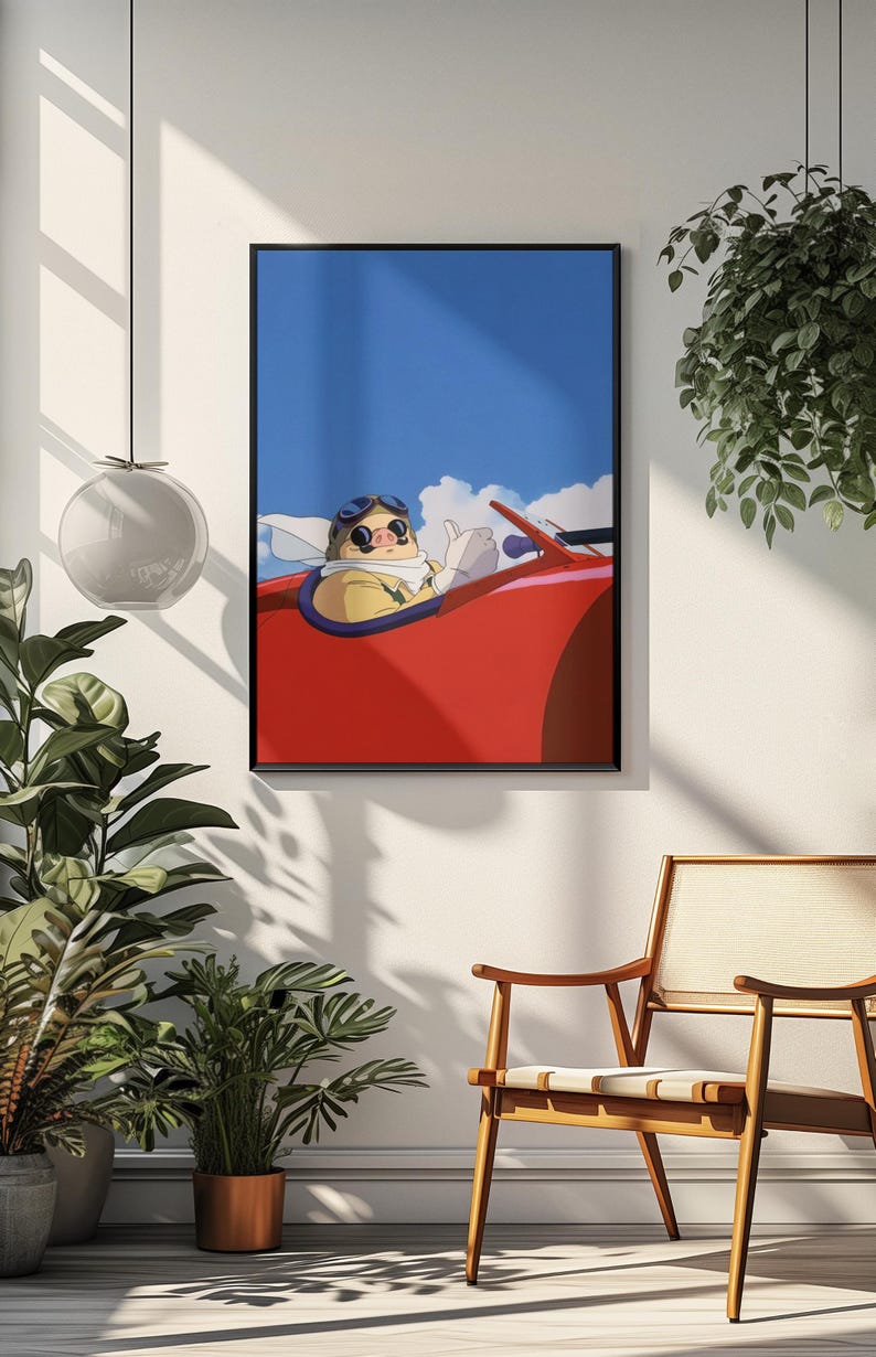 May include: Framed art print featuring a cartoon character in a red vintage car, set against a blue sky with clouds. The character wears goggles and a scarf, giving a thumbs-up. The artwork is displayed on a white wall.