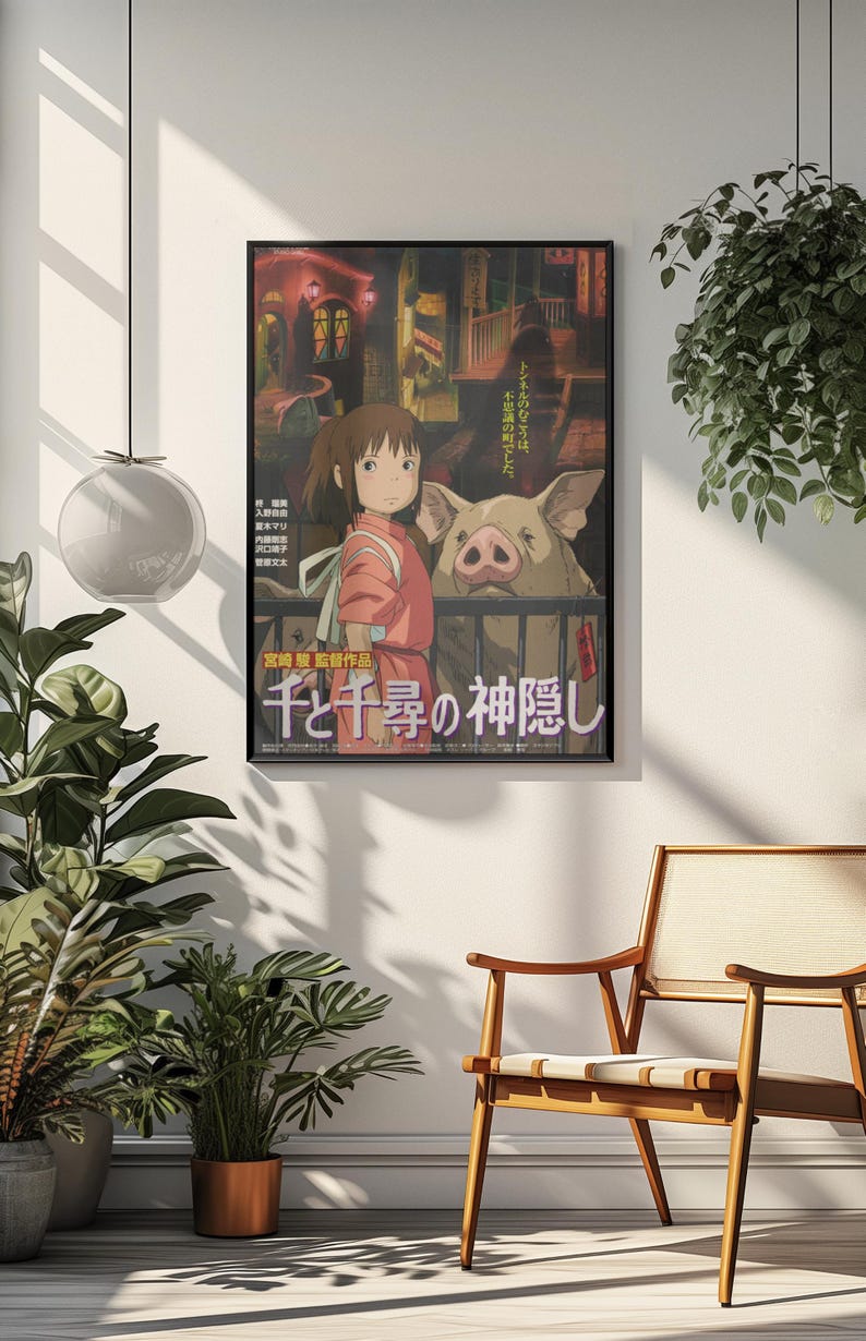 Op de afbeelding: Ingelijste poster met artwork uit de animatiefilm "Spirited Away". De poster toont een meisje in een rode outfit met een varken, met Japanse tekst. De poster wordt weergegeven op een witte muur.