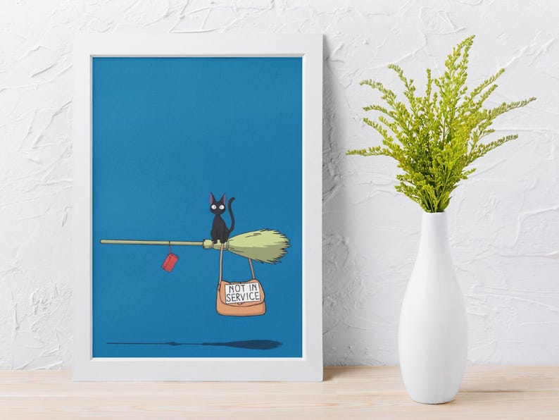 May include: A framed print featuring a black cat riding a broom against a blue background. The broom has a "Not in Service" sign and a red tag. A white vase with green foliage is on the right.