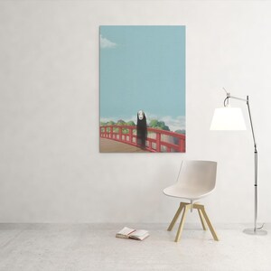 Op de afbeelding: Een ingelijste kunstdruk met een sc&egrave;ne uit de animatiefilm Spirited Away. Het kunstwerk toont een figuur op een rode brug tegen een blauwe lucht. Een moderne stoel, lamp en open boek staan op de voorgrond.
