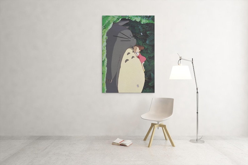 Pu&ograve; includere: Una stampa artistica incorniciata con una scena del film d'animazione, Il mio vicino Totoro. L'opera raffigura Totoro, un grande spirito della foresta grigio, con una bambina in un vestito rosa. Lo sfondo mostra un fogliame verde.