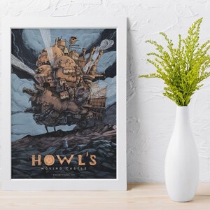 May include: A framed print of Howl's Moving Castle. The artwork depicts a detailed, steampunk-style castle floating in the sky, with a blue and gray background. The title "HOWL'S MOVING CASTLE" is displayed in gold lettering at the bottom of the print.