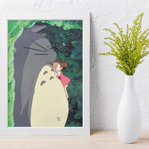 Pu&ograve; includere: Una stampa incorniciata con una scena del film d'animazione, Il mio vicino Totoro. L'opera raffigura una grande figura grigia di Totoro che abbraccia una ragazzina con un vestito rosso. Lo sfondo mostra un rigoglioso fogliame verde, con un vaso bianco e una pianta verde a destra.