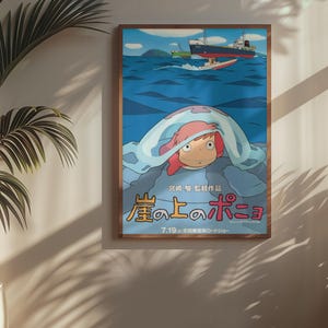 May include: A framed poster featuring a colorful illustration from the animated film "Ponyo." The artwork depicts a character with red hair under a blue blanket, with boats on the ocean in the background. The poster has Japanese text.