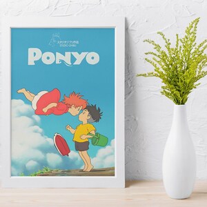 May include: Framed art print featuring the word "PONYO" in large, light blue letters against a blue sky background. The artwork depicts two animated characters, one in a red dress and the other in a yellow shirt, with a red surfboard and green bucket.