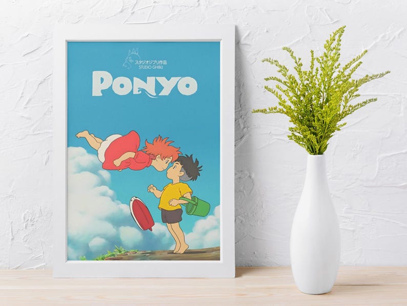 May include: Framed art print featuring the word "PONYO" in large, light blue letters against a blue sky background. The artwork depicts two animated characters, one in a red dress and the other in a yellow shirt, with a red surfboard and green bucket.
