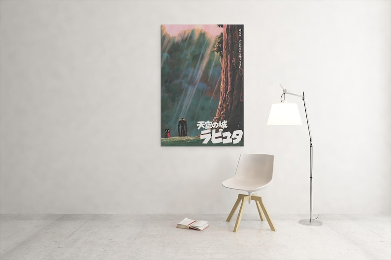 May include: A framed poster with Japanese text and artwork from the animated film "Castle in the Sky." The artwork shows a forest scene with figures and a large tree. The poster is mounted on a white wall.