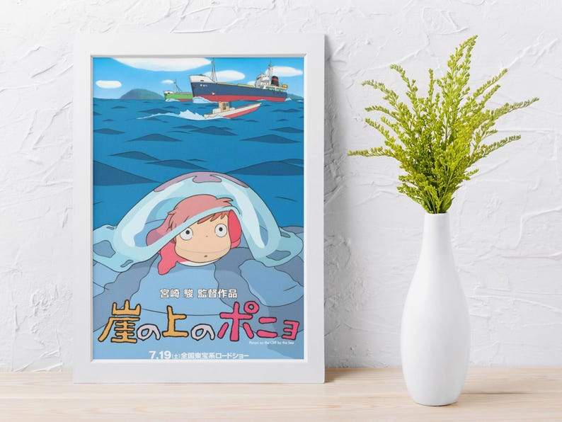 May include: Framed poster featuring a cartoon illustration of a character with pink hair under a blue wave, with ships on the ocean. The poster has Japanese text and is in a white frame. A white vase with green foliage is to the right.