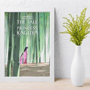 May include: A framed print of "The Tale of the Princess Kaguya" features a woman in a pink kimono walking through a bamboo forest. The print is in a white frame and is set on a wooden surface. A white vase holds green foliage.