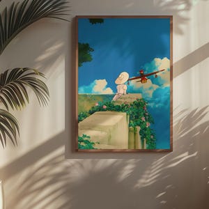 May include: A framed art print depicts a serene scene with a person in a white hat sitting on a stone wall, overlooking a blue sky with fluffy clouds. A red airplane flies nearby. The artwork is framed in a brown wooden frame.