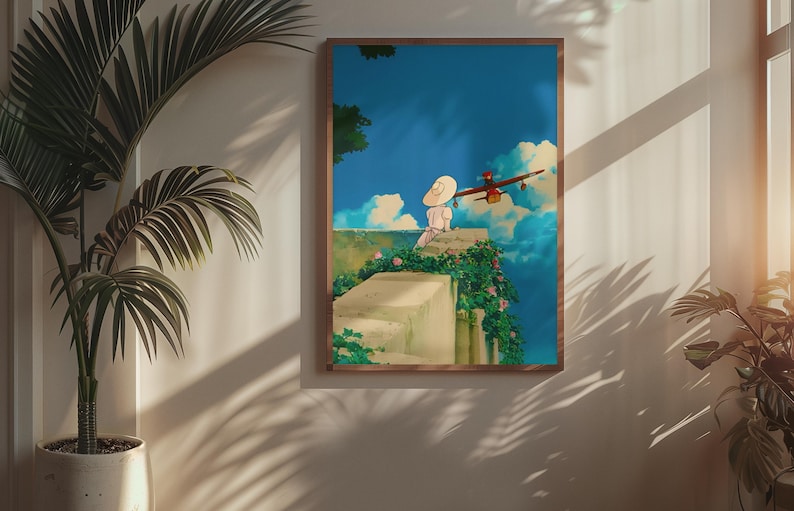 May include: A framed art print depicts a serene scene with a person in a white hat sitting on a stone wall, overlooking a blue sky with fluffy clouds. A red airplane flies nearby. The artwork is framed in a brown wooden frame.
