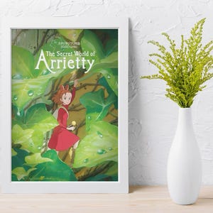 May include: Framed poster of "The Secret World of Arrietty" featuring a young girl in a red dress amidst lush green foliage. The poster is in a white frame, and a white vase with green sprigs sits nearby.