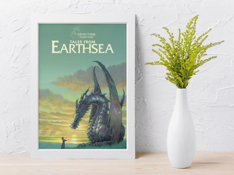 May include: A framed poster featuring the "Tales from Earthsea" movie. The artwork depicts a large, detailed dragon with a person in the foreground, set against a sunset sky. The poster is in a white frame, with a white vase and green plant to the right.
