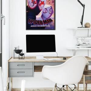 May include: A framed poster featuring the animated film "Spider-Man: Across the Spider-Verse." The poster showcases two Spider-Man characters in a dynamic pose, with the film's title prominently displayed. The poster is hanging above a desk with a computer and a white chair.