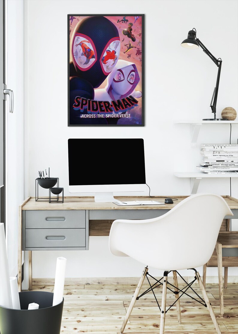 May include: A framed poster featuring the animated film "Spider-Man: Across the Spider-Verse." The poster showcases two Spider-Man characters in a dynamic pose, with the film's title prominently displayed. The poster is hanging above a desk with a computer and a white chair.
