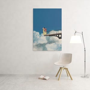 May include: A framed art print depicts a person on a bridge above clouds against a blue sky. The artwork is displayed on a white wall, with a modern chair, a floor lamp, and a book in the foreground.