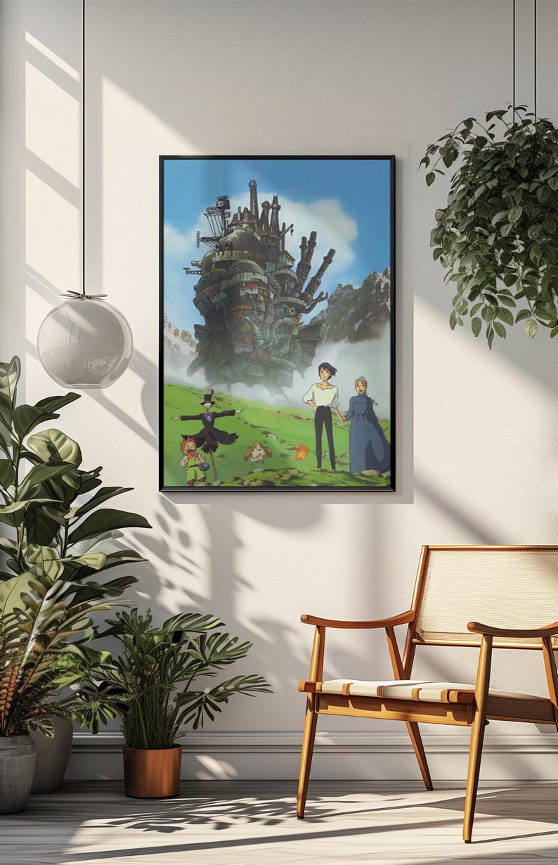 May include: Framed art print featuring a scene from the animated film, Howl's Moving Castle. The artwork depicts the castle, characters, and a green landscape under a blue sky. The print is displayed on a white wall, with a wooden chair and plants in the foreground.