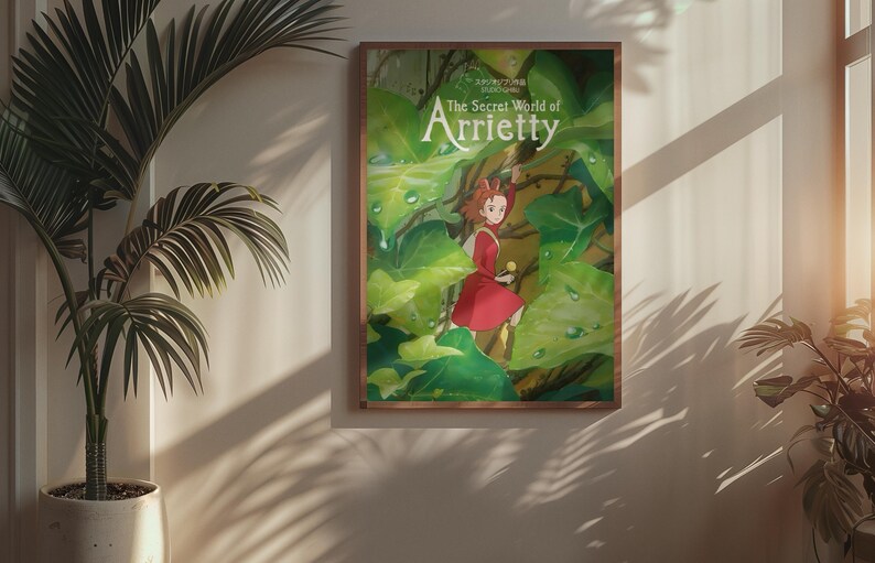May include: A framed poster of "The Secret World of Arrietty" anime film. The artwork features a young girl in a red dress amidst lush green foliage. The poster is in a wooden frame, hanging on a wall with a potted plant.