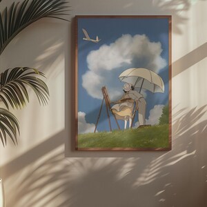 May include: A framed art print depicts a person painting outdoors under an umbrella. The artwork features a blue sky with fluffy clouds and a small airplane. The print is in a wooden frame and hangs on a white wall.