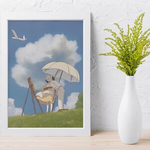 May include: A framed art print featuring an animated scene of two figures painting outdoors under a parasol. The artwork depicts a sunny day with a blue sky, fluffy clouds, and a grassy hill. A white vase with green foliage is on the right.