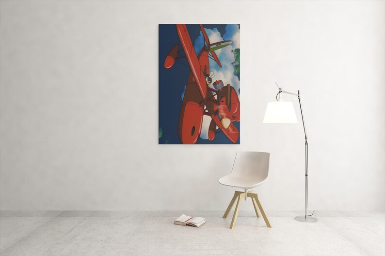 May include: A framed art print featuring a red airplane against a blue sky with clouds. The artwork is displayed on a white wall, with a modern chair and a floor lamp in the foreground. A book is open on the floor.