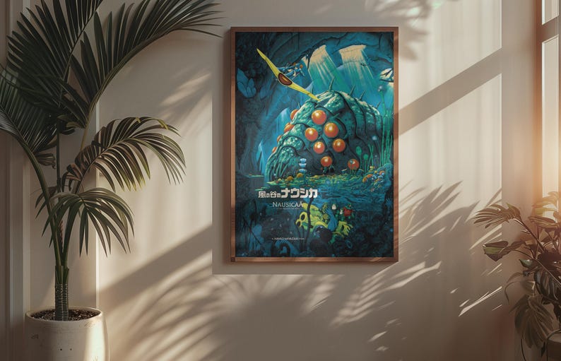 Puede incluir: P&oacute;ster enmarcado con una ilustraci&oacute;n de "Nausica&auml; del Valle del Viento". Muestra una criatura bulbosa con esferas naranjas sobre un fondo azul y verde. Texto japon&eacute;s visible. Marco de madera marr&oacute;n.