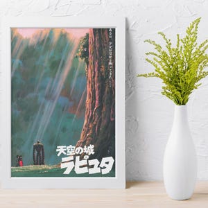May include: A framed poster with Japanese text and artwork from the animated film "Castle in the Sky." The poster is in a white frame and shows a tall tree, a robot, and two small figures in a colourful, vibrant scene.