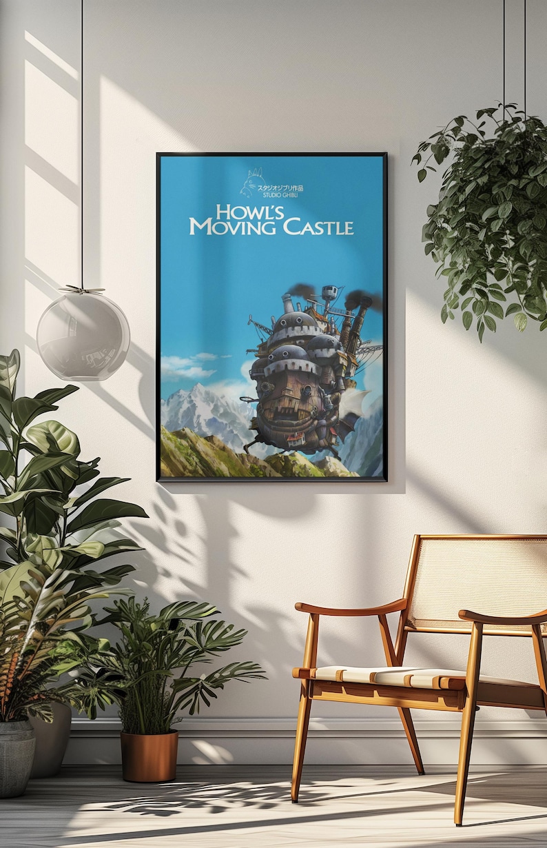 May include: Framed poster featuring the animated film "Howl's Moving Castle." The artwork depicts the castle in motion against a blue sky and mountain backdrop. The poster has a black frame and is displayed in a well-lit room with plants and a wooden chair.